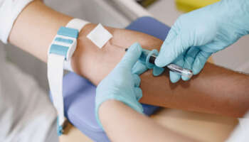 Skillful nurse is doing blood test for man in clinic. Man in a medical mask.