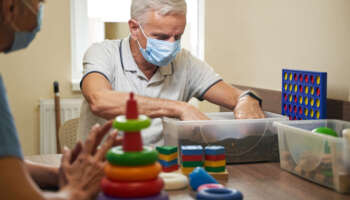 Mature male patient in medical mask performing activities for recovery of adaptive skills in rehab center