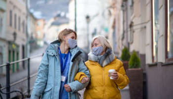 Senior woman with caregiver or healthcare worker outdoors on a walk in town, coronavirus concept.