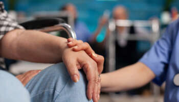 Social assistant worker consoling handicapped pensioner patient touching hands during homecare service. Healthcare support assistance. Social services nursing at home. Caregiver nurse